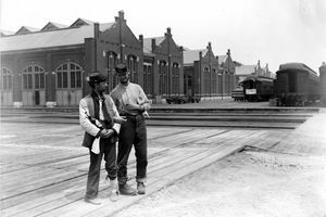 Двама военнослужещи стоят до сградата на Пулман и тренират автомобили със заключени ръце и бутилка алкохол по време на стачката в Чикаго от Пулман от 1894 г.