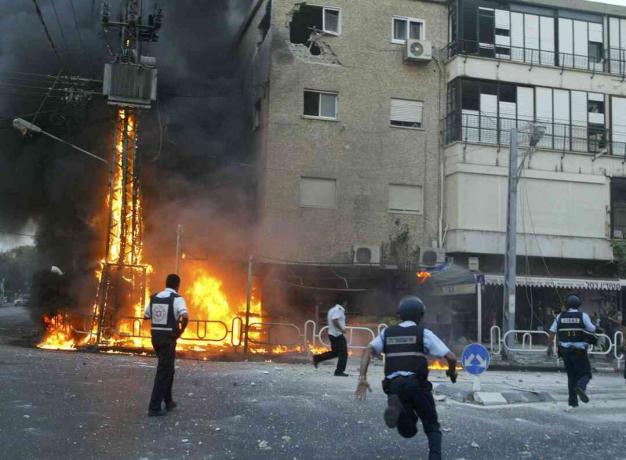 6. Израелски полицаи се втурват към мястото на горящ електрически пилон и повредени сградни моменти, след като залп от ракети "Хизбула" удари 13 юли 2006 г. в северния град Нахария, Израел.