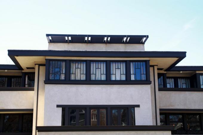 хоризонтално ориентирана светлолинейна къща с тъмно кафява облицовка, плосък покрив с огромни надвеси и редици прозорци с оловно стъкло