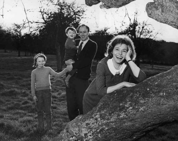 Черно-бяла снимка на Роалд Дал, който държи децата си; съпругата му Патриша Нийл се обляга на дърво