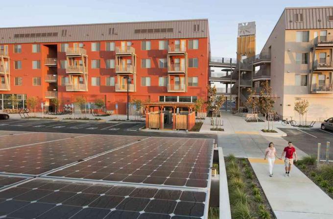 Двама души, които се разхождат в близост до зелени сгради и слънчеви панели, в общност Zero Net Energy