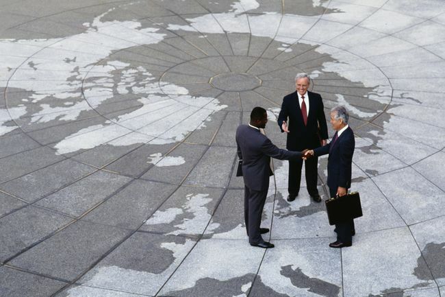  Икономически регионализъм: Бизнесмени се ръкуват върху картата на земното кълбо.