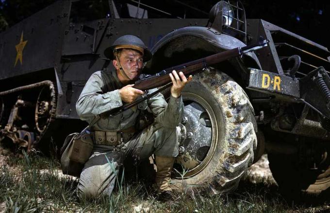 Американски войник коленичи с M1 Garand пред халфрак.
